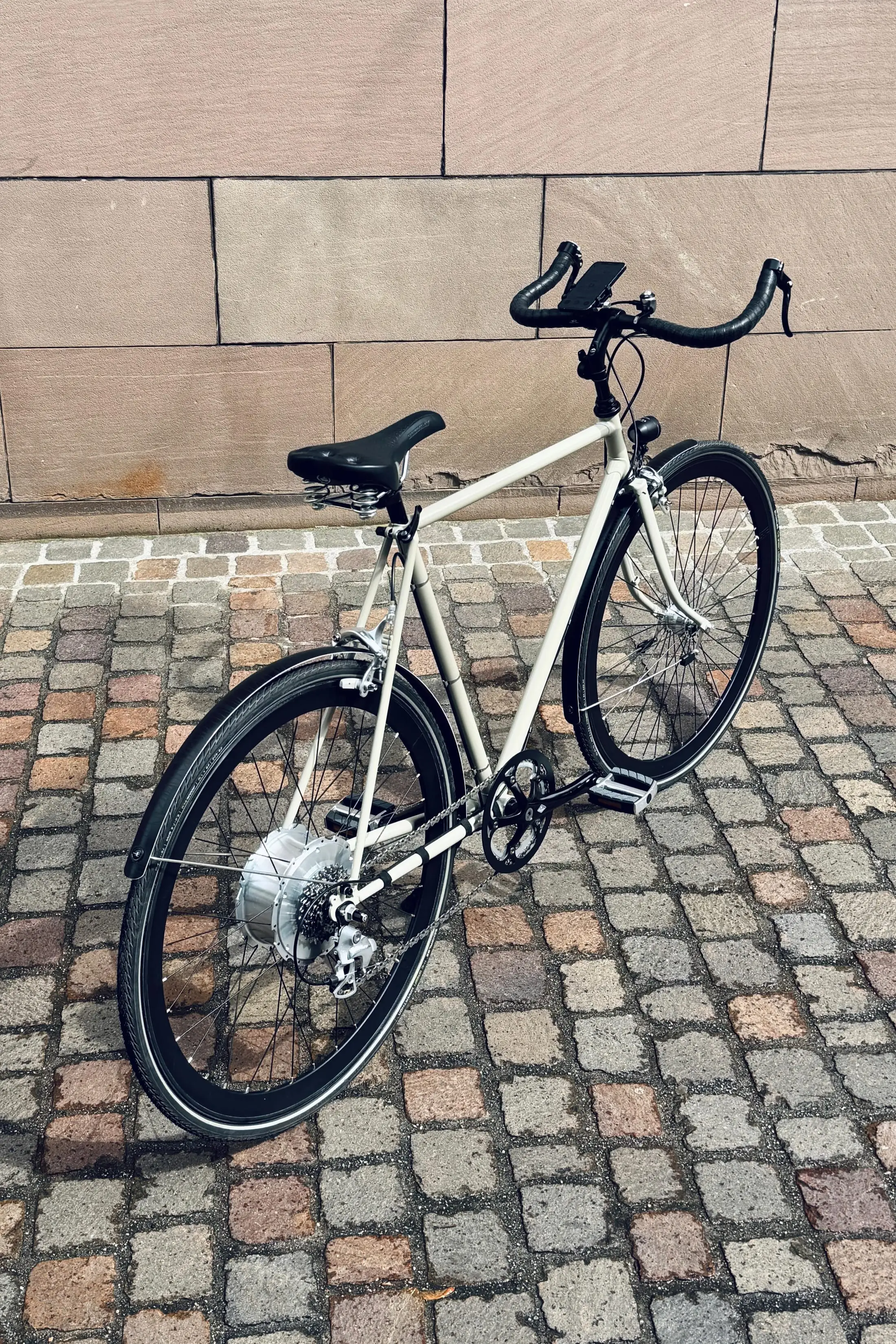 Cremefarbenes Stadtvelo mit Rennlenker und Zehus-Nabenmotor im Hinterrad, abgestellt auf Basler Kopfsteinpflaster